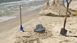 Une plage de sable avec un grand château de sable, une pelle et un seau.
