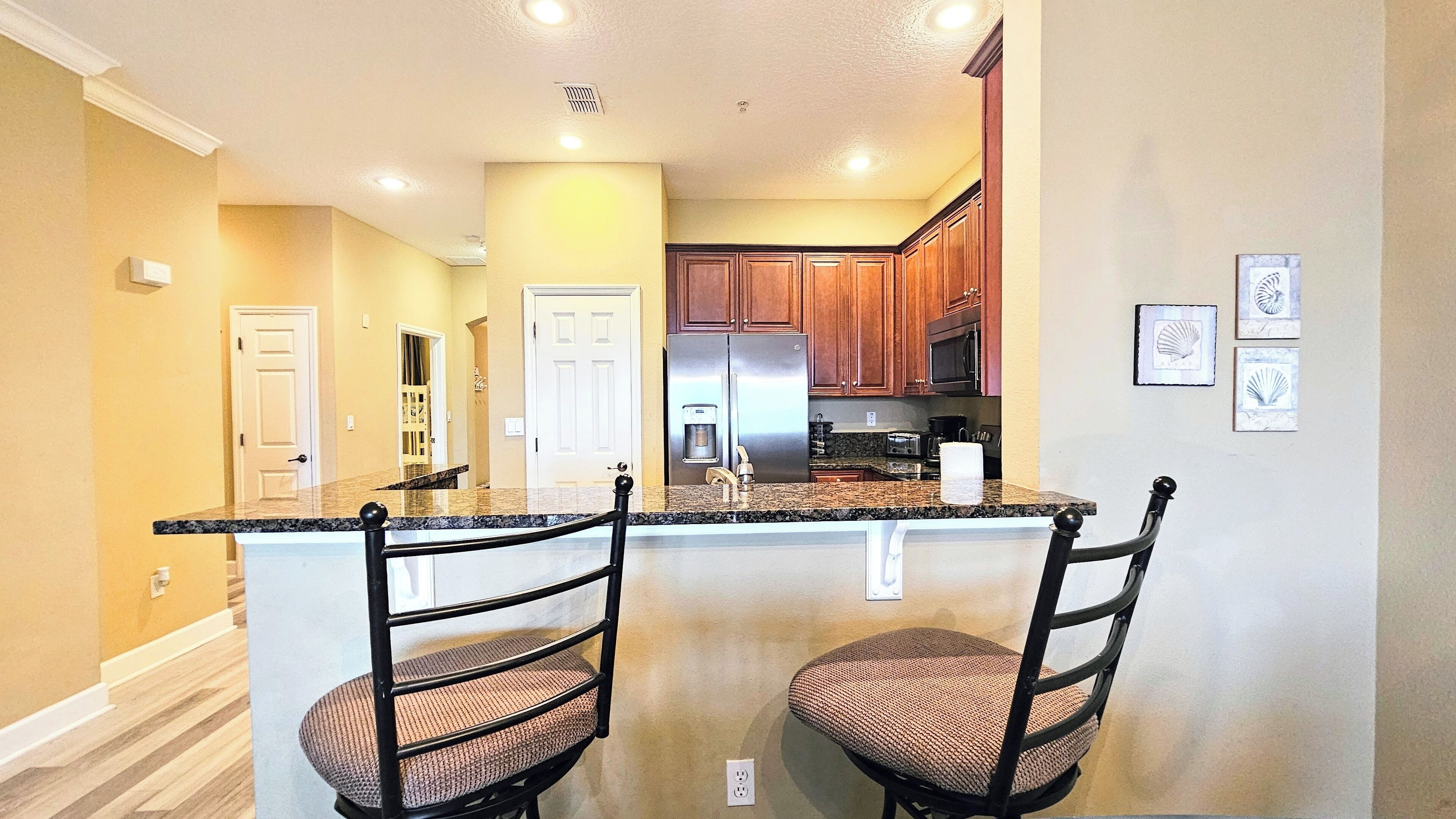 A kitchen with granite countertops, stainless steel appliances, wooden cabinets, and two bar stools.
