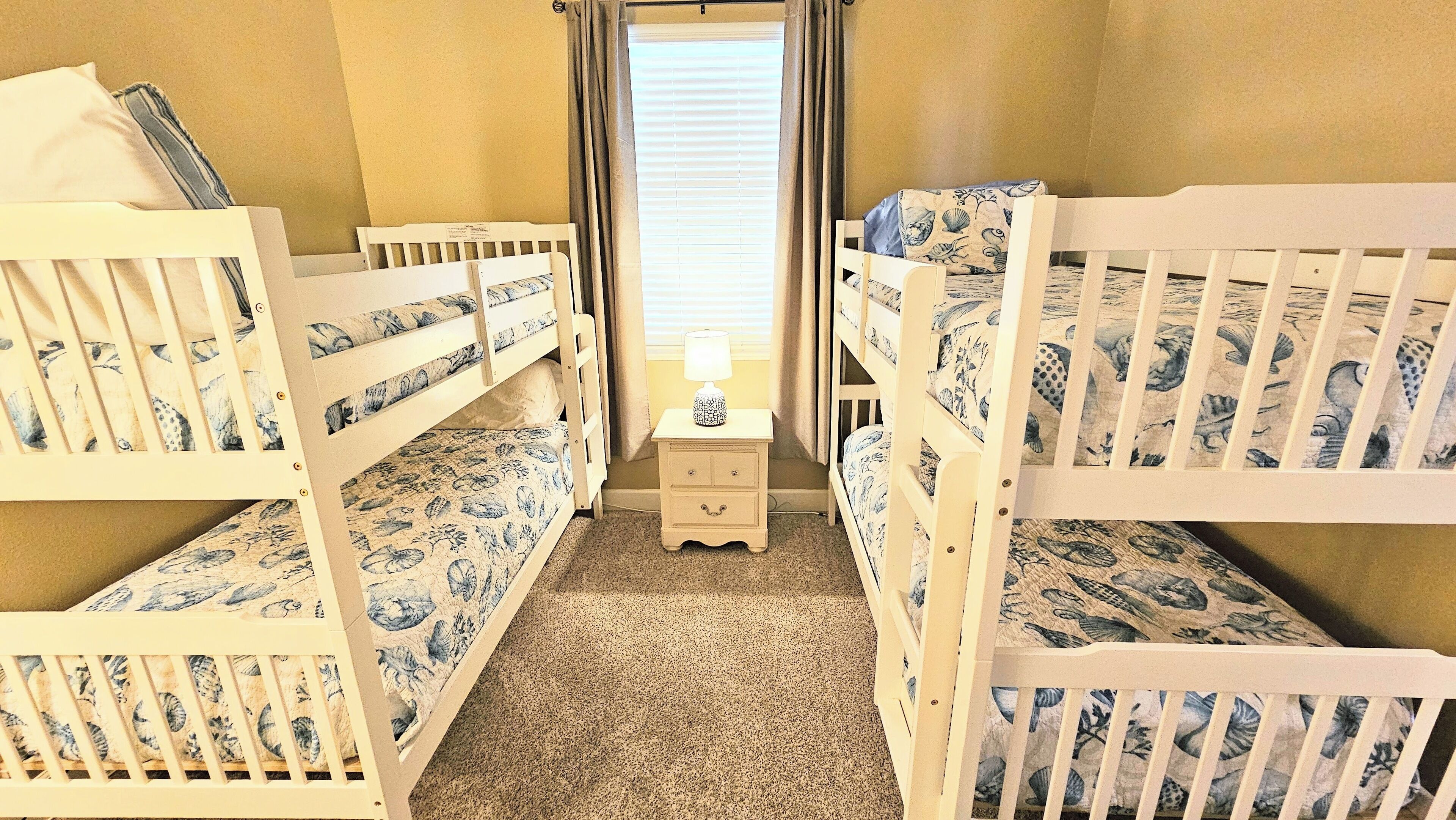 A room with bunk beds, a nightstand with a lamp, and a window with curtains.
