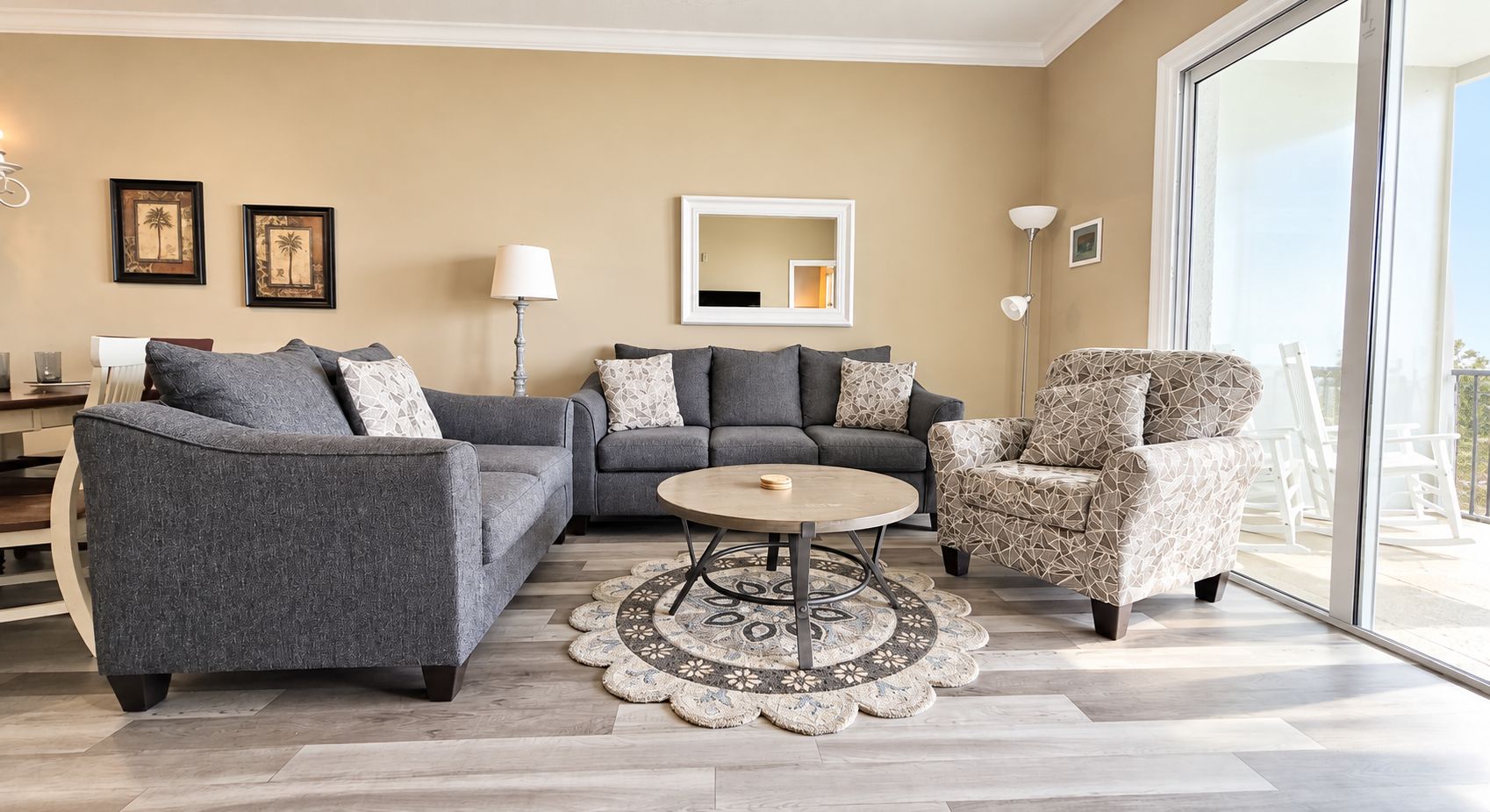 A living room with a grey sofa, a patterned armchair, a round coffee table, and a large window with a view.