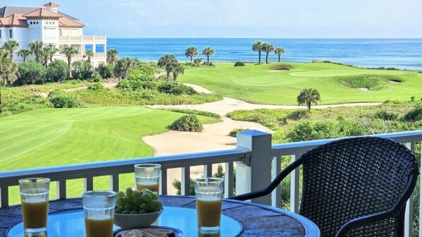 Un balcon avec une table et des chaises donnant sur un terrain de golf et l’océan.