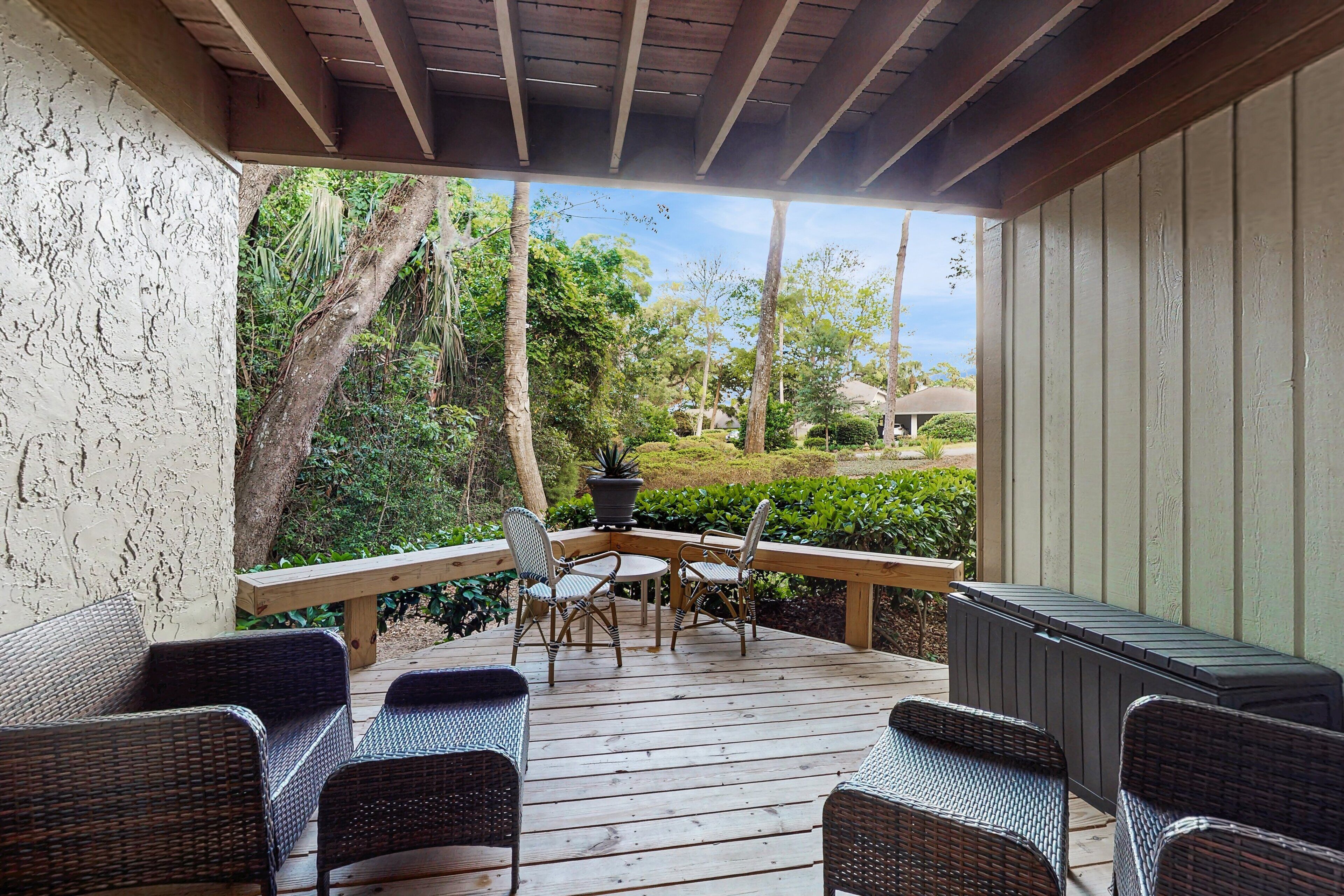 A covered outdoor deck with wicker furniture, a table, and a potted plant.