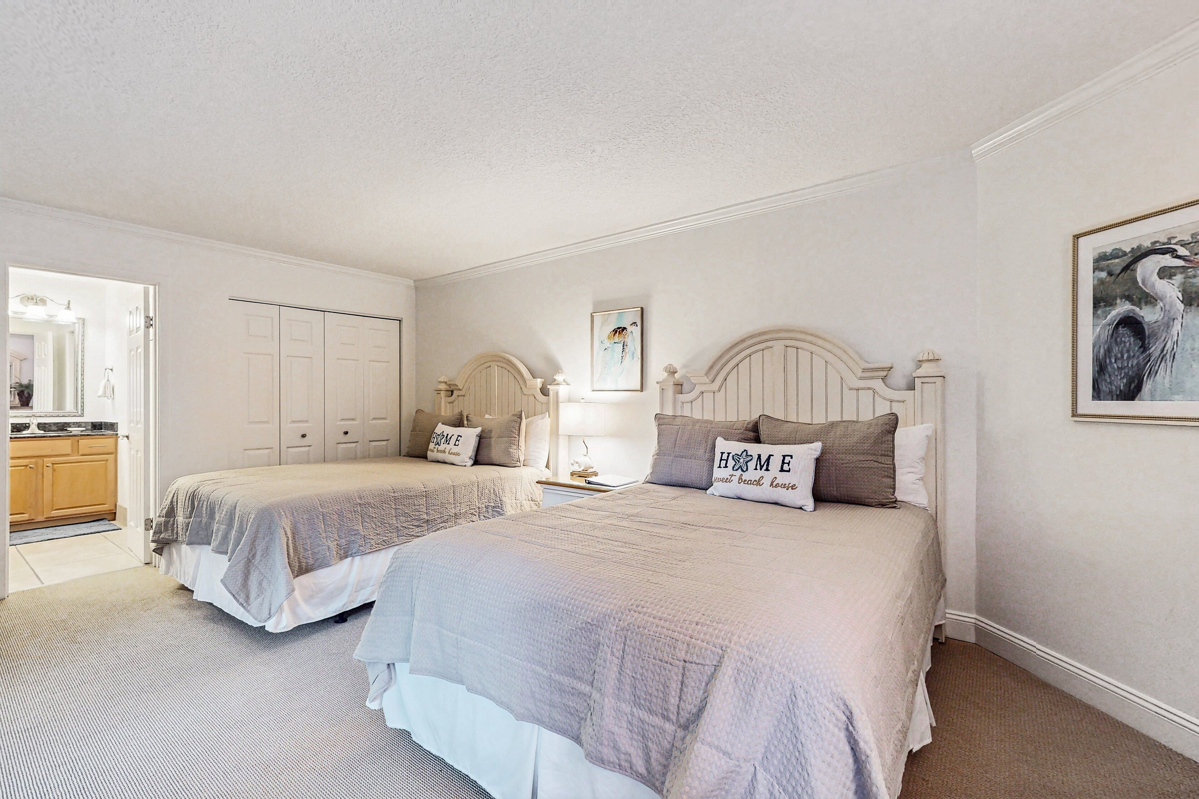 Een slaapkamer met twee bedden, een houten garderobe, een schilderij en uitzicht op de keuken.