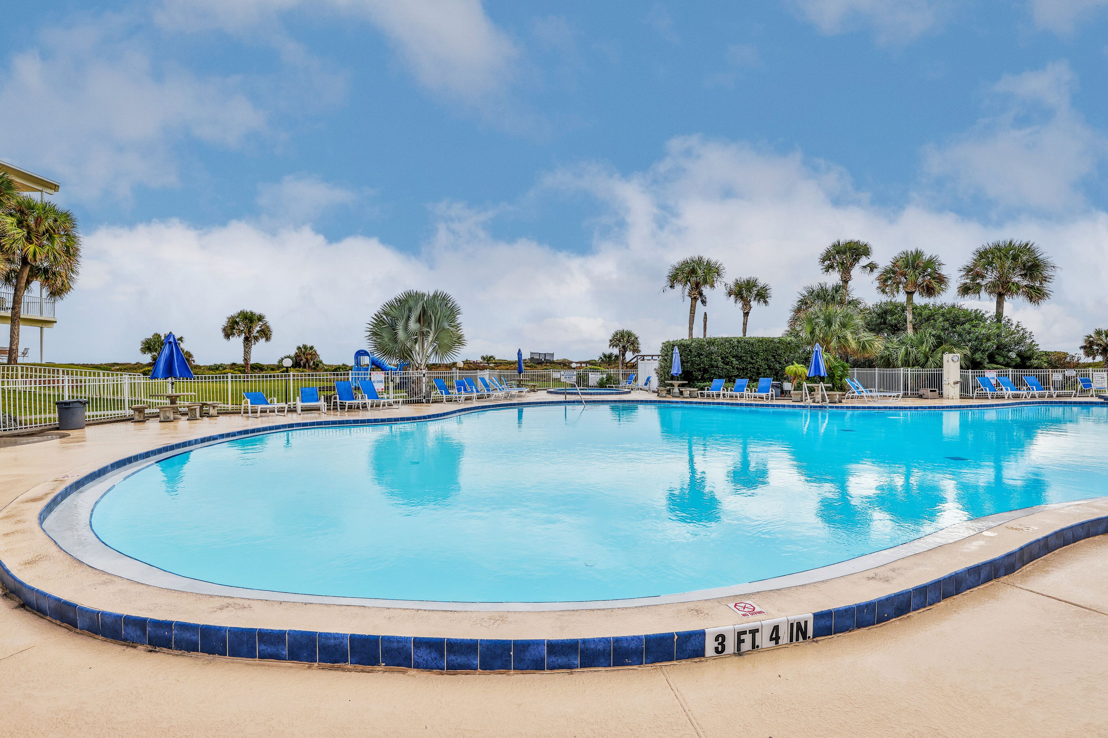 A swimming pool with a blue tiled edge, surrounded by lounge chairs and palm trees.