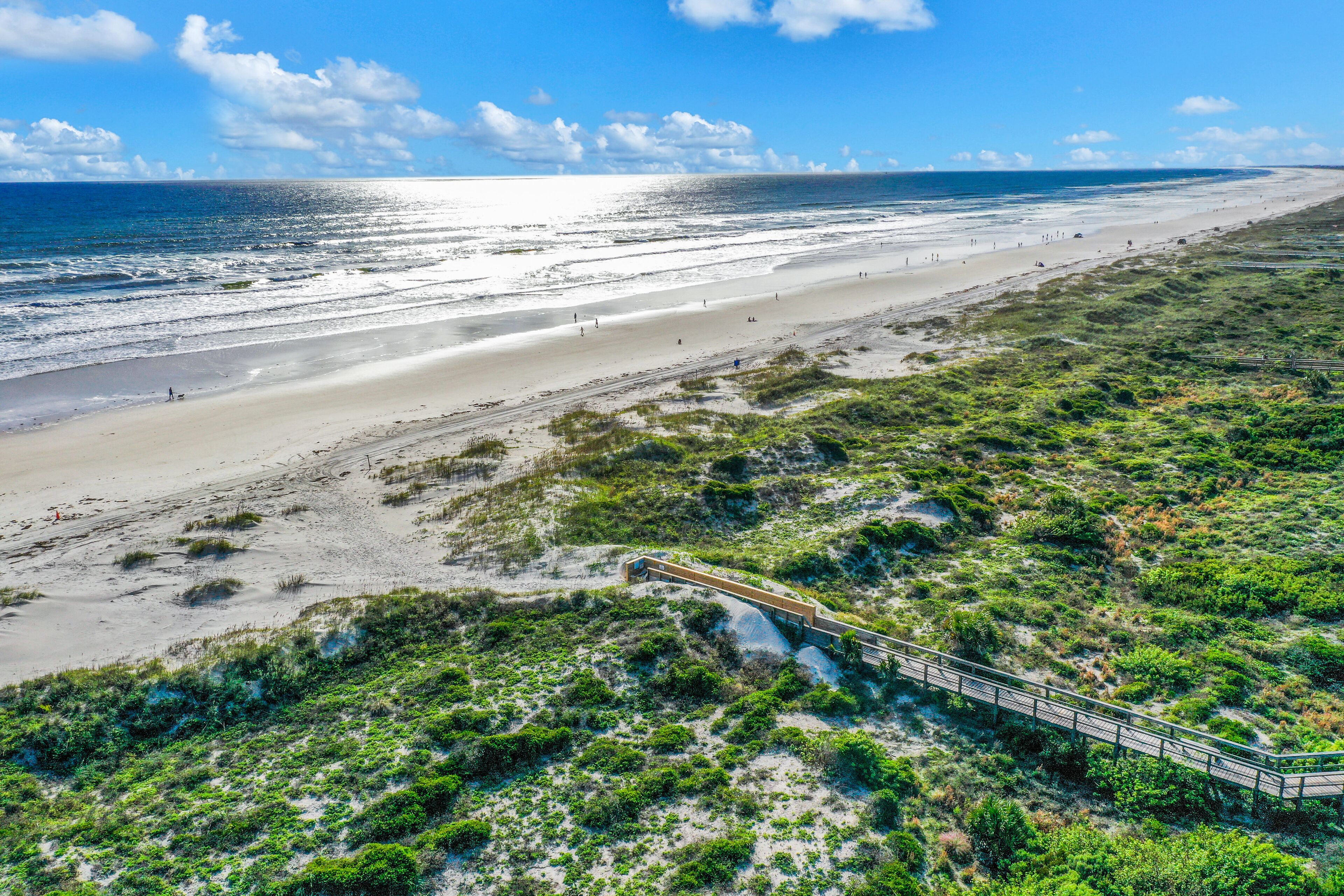 A beach with a wooden boardwalk leading to the water, sandy dunes, and a clear sky.
