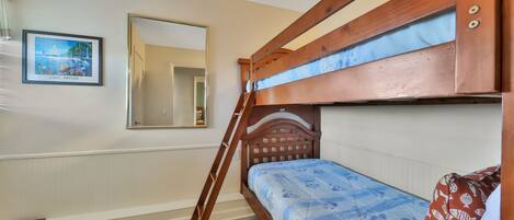 Una cama litera con escalera de madera, un cuadro en la pared y un espejo.