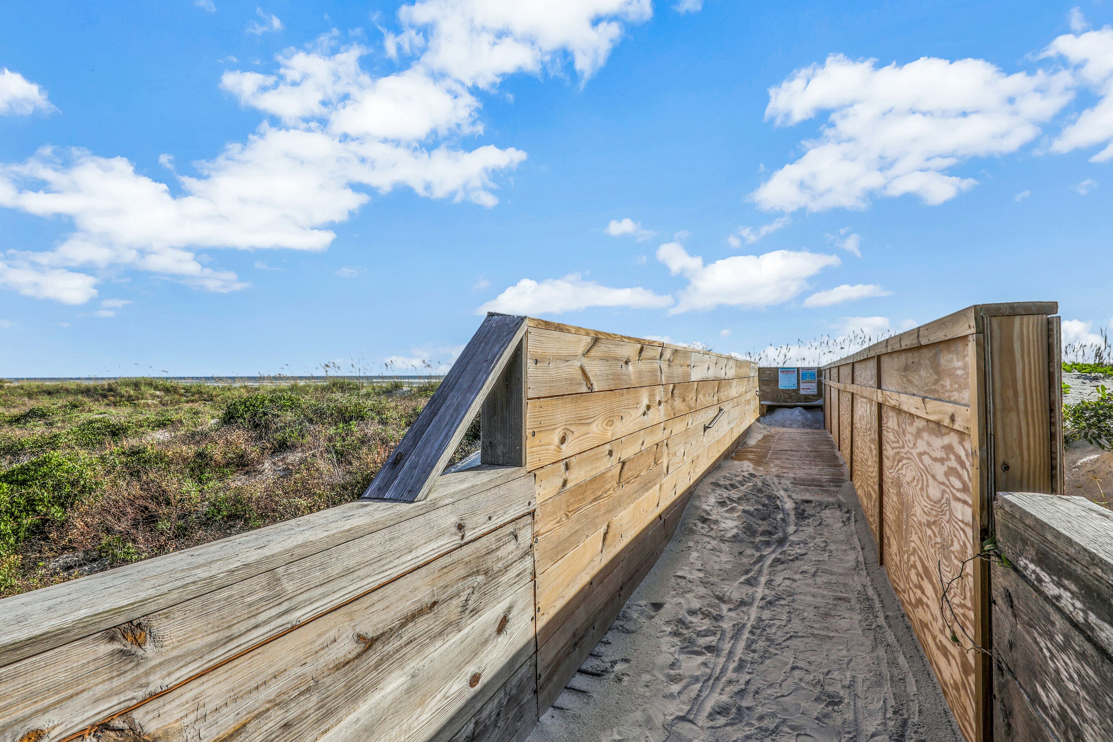 A wooden boardwalk leading to a beach with a clear sky.