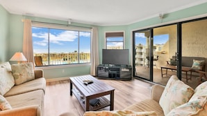 A living room with a sofa, a coffee table, a TV, and a sliding glass door leading to an outdoor area. - Beautiful Home Near the Beach With Views of the Atlantic off the Private Balcony (St. Augustine)