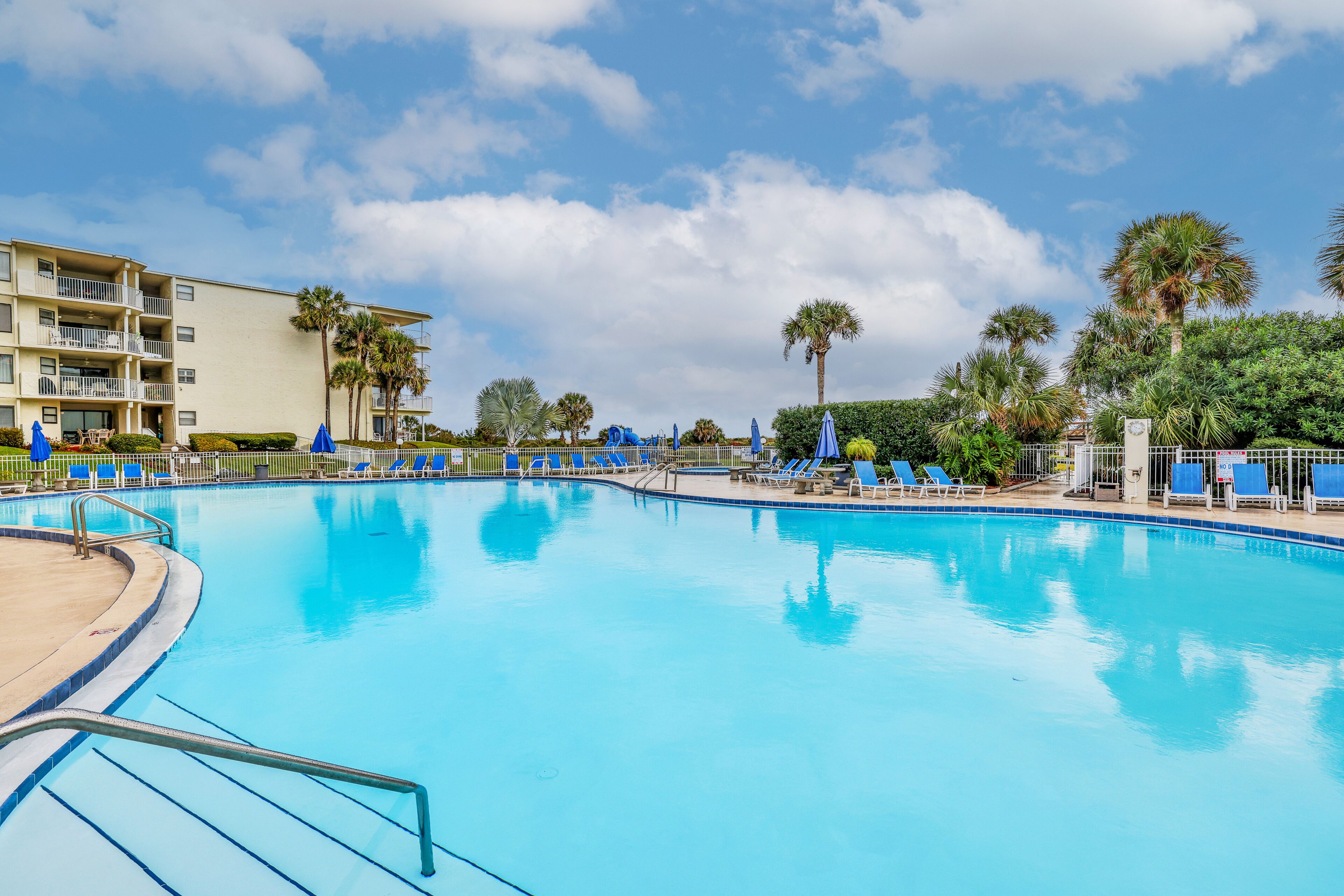 Ein Swimmingpool mit blauem Wasser, umgeben von Liegestühlen und Palmen.