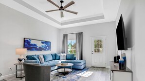 A modern living room with a blue sofa, a round coffee table, and a ceiling fan. - All-new Duplex With Screened Pool, Furnished Lanai, Grill, AC, & Washer/dryer (Palm Coast)
