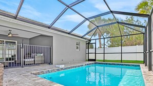 A covered swimming pool with a glass ceiling, a patio area with seating, and a view of the surrounding greenery. - All-new Duplex With Screened Pool, Furnished Lanai, Grill, AC, & Washer/dryer (Palm Coast)