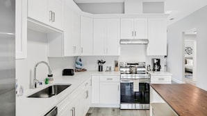 A modern kitchen with white cabinetry, stainless steel appliances, and a wooden countertop. - All-new Duplex With Screened Pool, Furnished Lanai, Grill, AC, & Washer/dryer (Palm Coast)