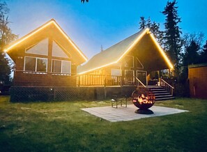 A two-story house with a covered porch and a fire pit in the yard. - The Kenai River Cabin Collection (Soldotna)