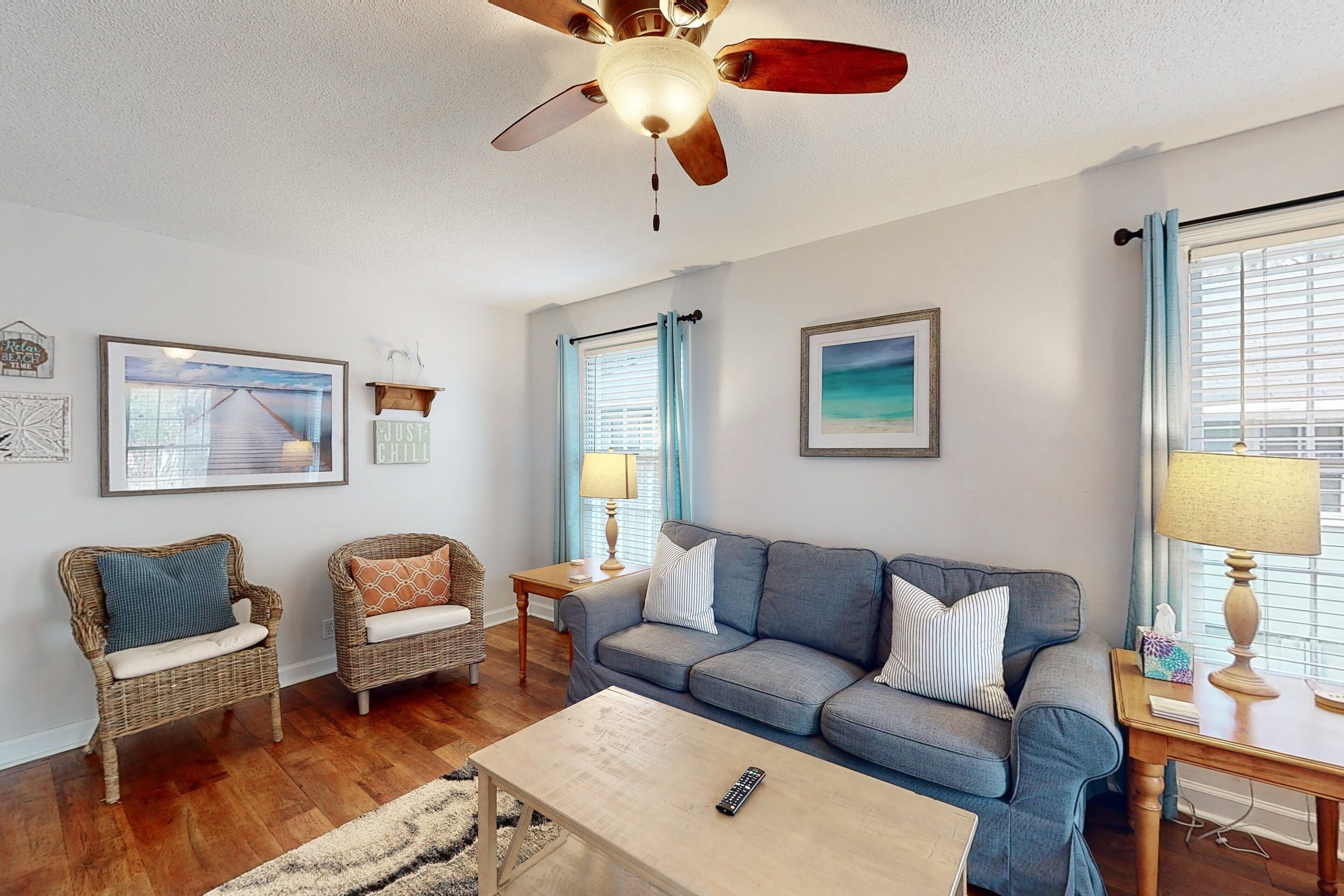 A living room with a ceiling fan, wicker chairs, a sofa, a coffee table, and framed pictures on the walls.