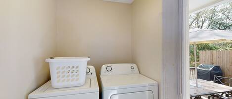 A laundry area with two white washing machines and a white laundry basket on top of the left machine.