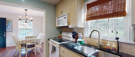 A kitchen with a stove, microwave, sink, and dining area with chairs.