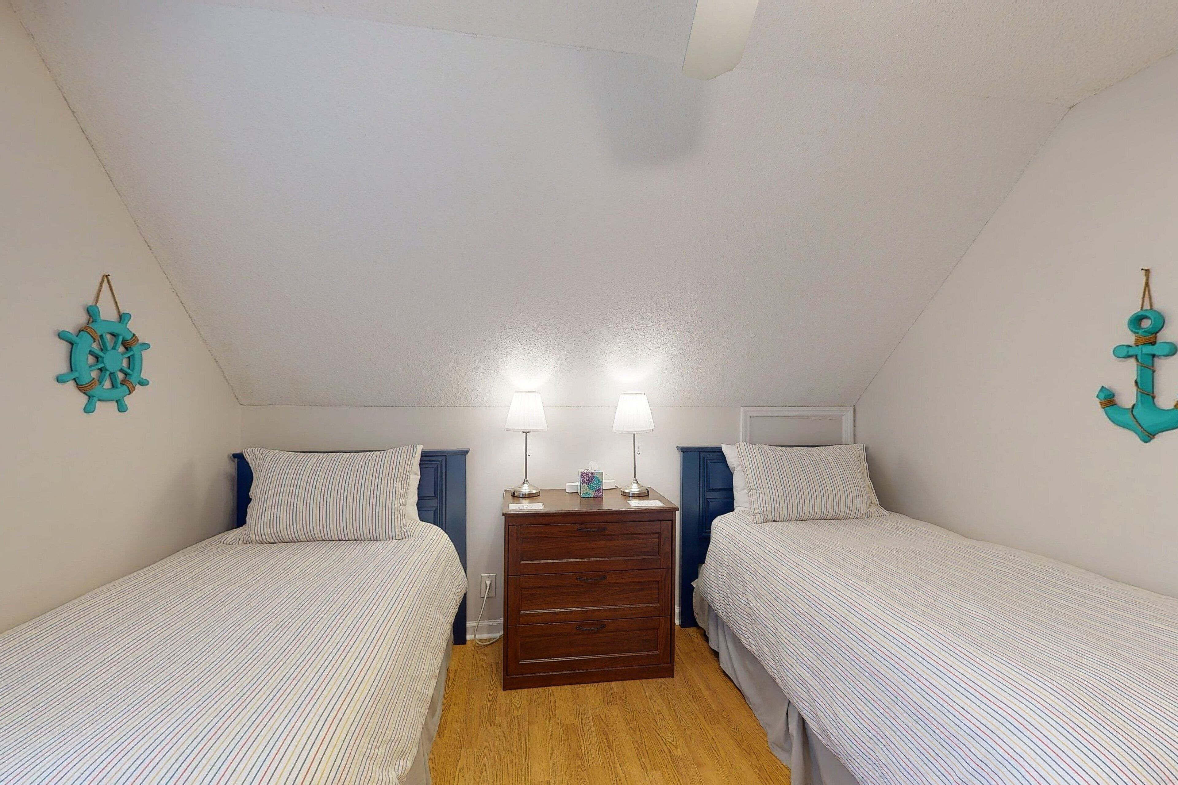 A small, cozy bedroom with two single beds, a wooden dresser, and a ceiling fan.