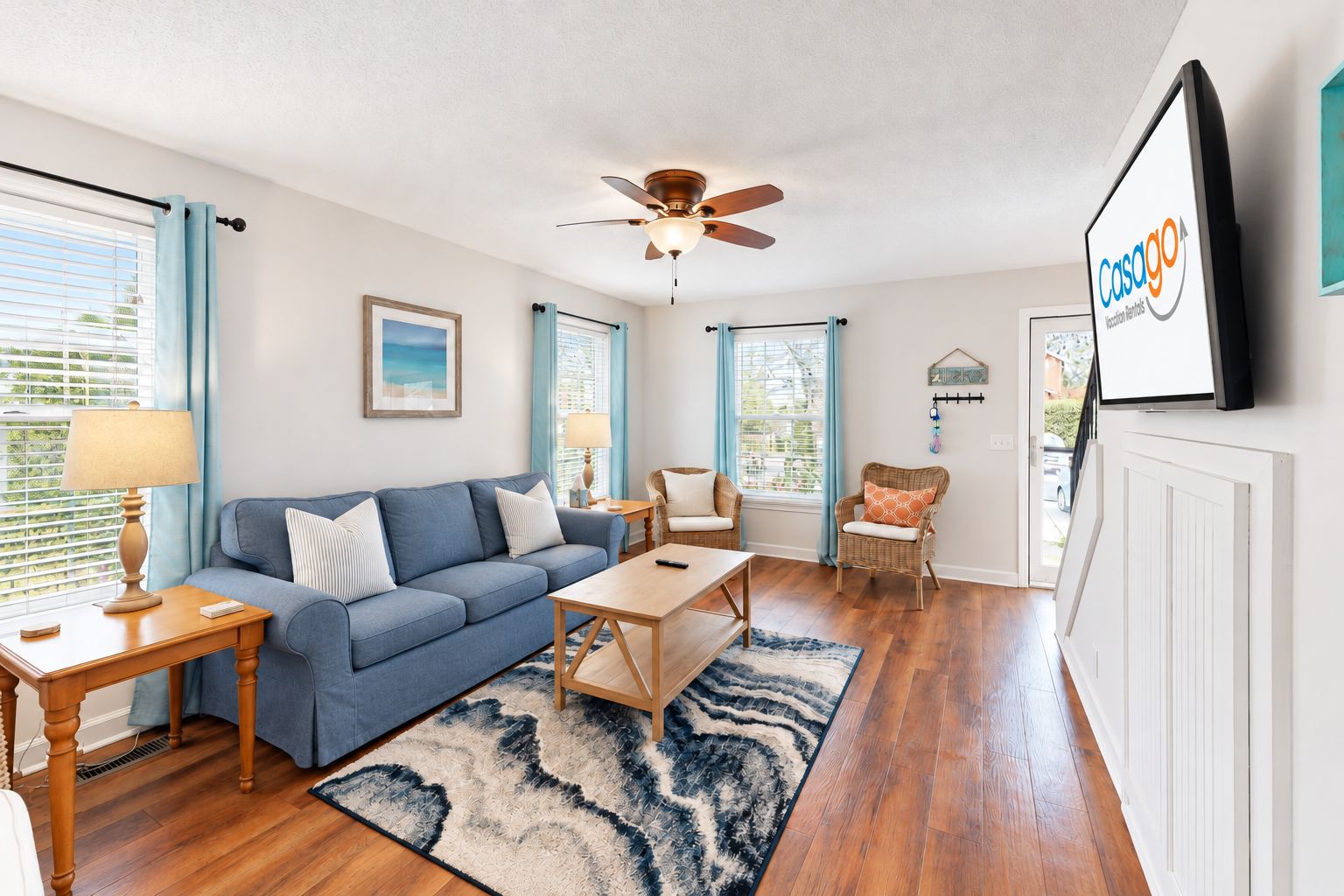 Een woonkamer met een blauwe bank, een houten salontafel en een plafondventilator.