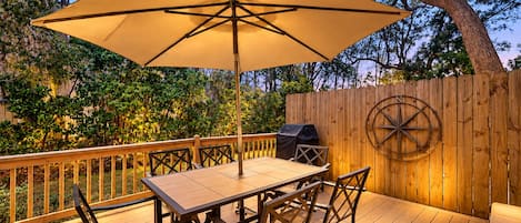 Una terrazza esterna con tavolo e sedie, un ombrellone grande e un recinto in legno con una bussola.