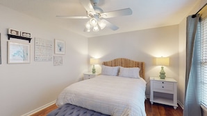 Ein Schlafzimmer mit einem Bett, zwei Nachttischen, einem Deckenventilator und Wandbildern.