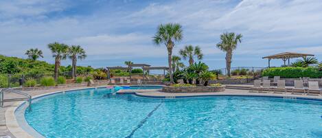 A swimming pool with clear blue water, surrounded by palm trees and lounge chairs.