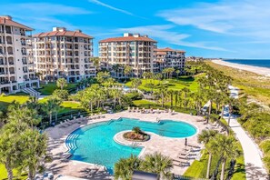 Un resort con varias edificaciones, una piscina central y vista a la playa.