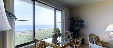 A room with a balcony, a table with chairs, a sofa, and a potted plant.