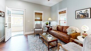 A living room with a brown leather sofa, a glass coffee table, a wooden chair, and a ceiling fan. - Classy Cottage With a Washer/dryer, Central AC, & Fast Wifi - Near Beaches (St. Augustine)