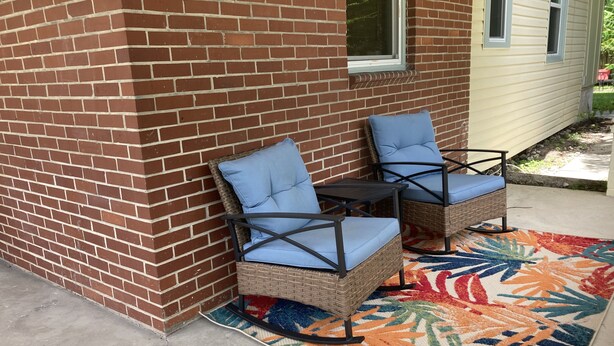 A patio area with two wicker chairs with blue cushions, a small table, and a colorful rug. - Classy Cottage With a Washer/dryer, Central AC, & Fast Wifi - Near Beaches (St. Augustine)