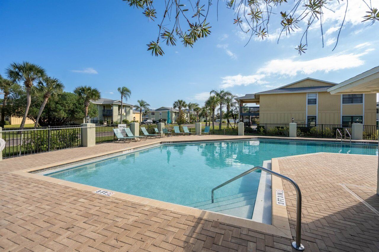 A swimming pool with lounge chairs, palm trees, and a building in the background.