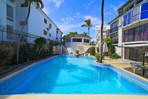 A swimming pool with clear blue water, surrounded by white buildings with balconies and palm trees. -  1-bedroom apartment  central Sosua. No Car or scooter need. Close to everything (Sosúa)