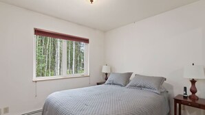 A bedroom with a large bed, two bedside lamps, a window with a view of trees, and a ceiling light.