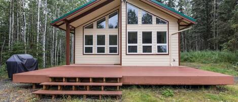 A cabin with a porch, large windows, and a covered grill area.