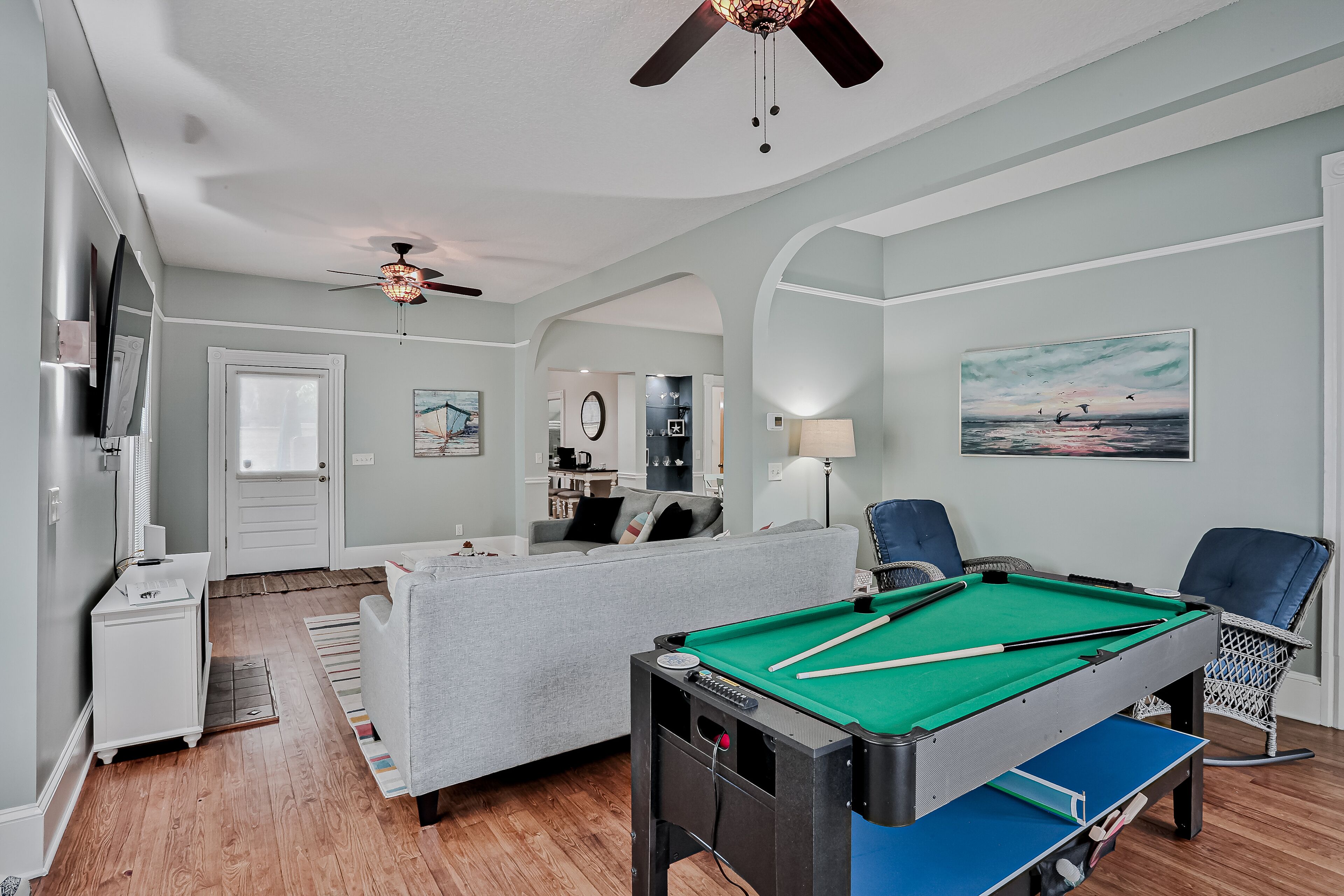 A modern living room with a pool table, a sofa, and a ceiling fan.