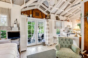 A cozy room with a bed, a desk, a chair, and a television. There are open doors leading to an outdoor area with a table and chairs. - Charming Getaway w/ a Kitchenette & Free Wifi - Walk to the Beach (St. Simons Island)