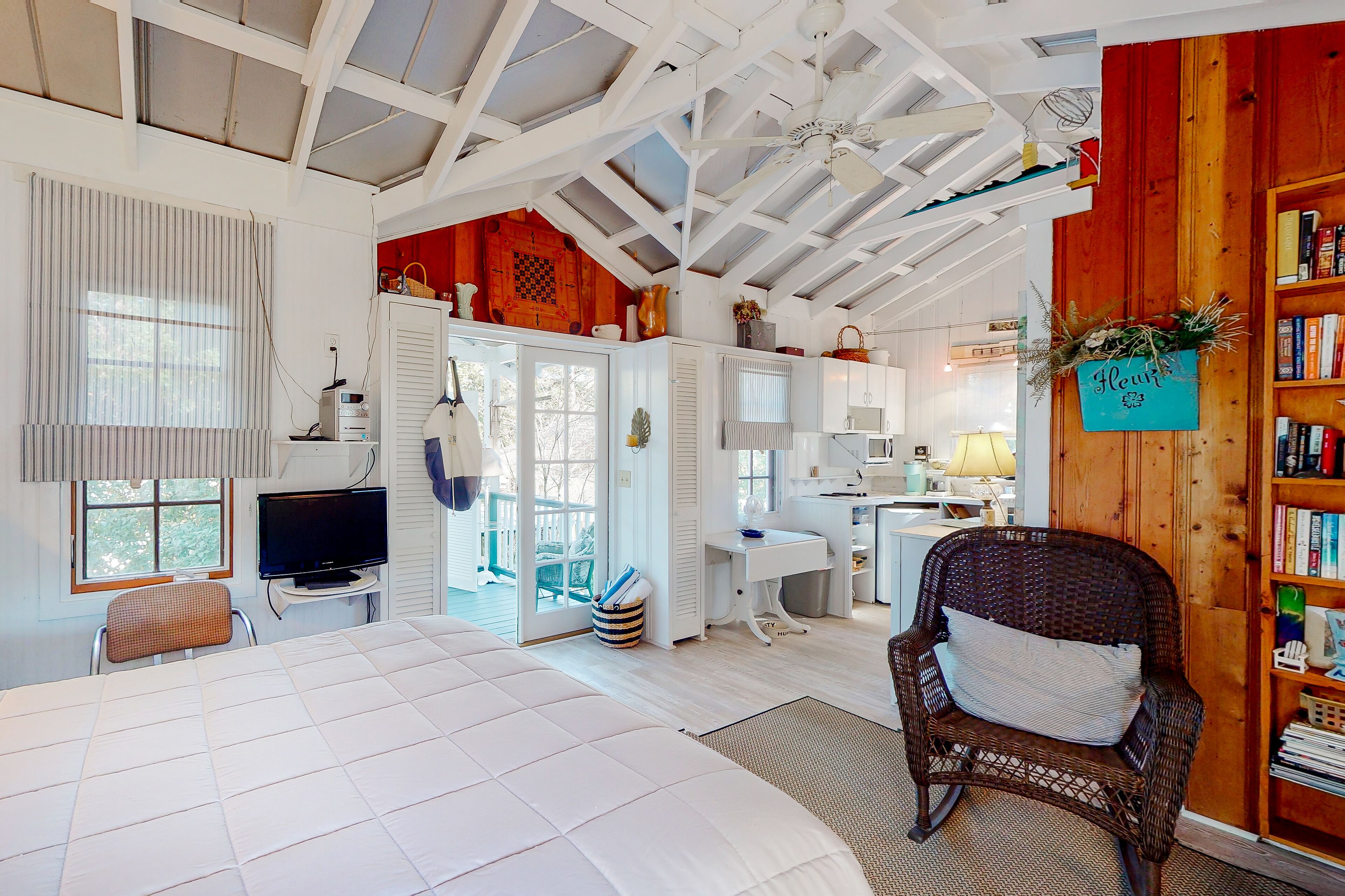 A bedroom with a large bed, a television, and a wicker chair with a pillow.