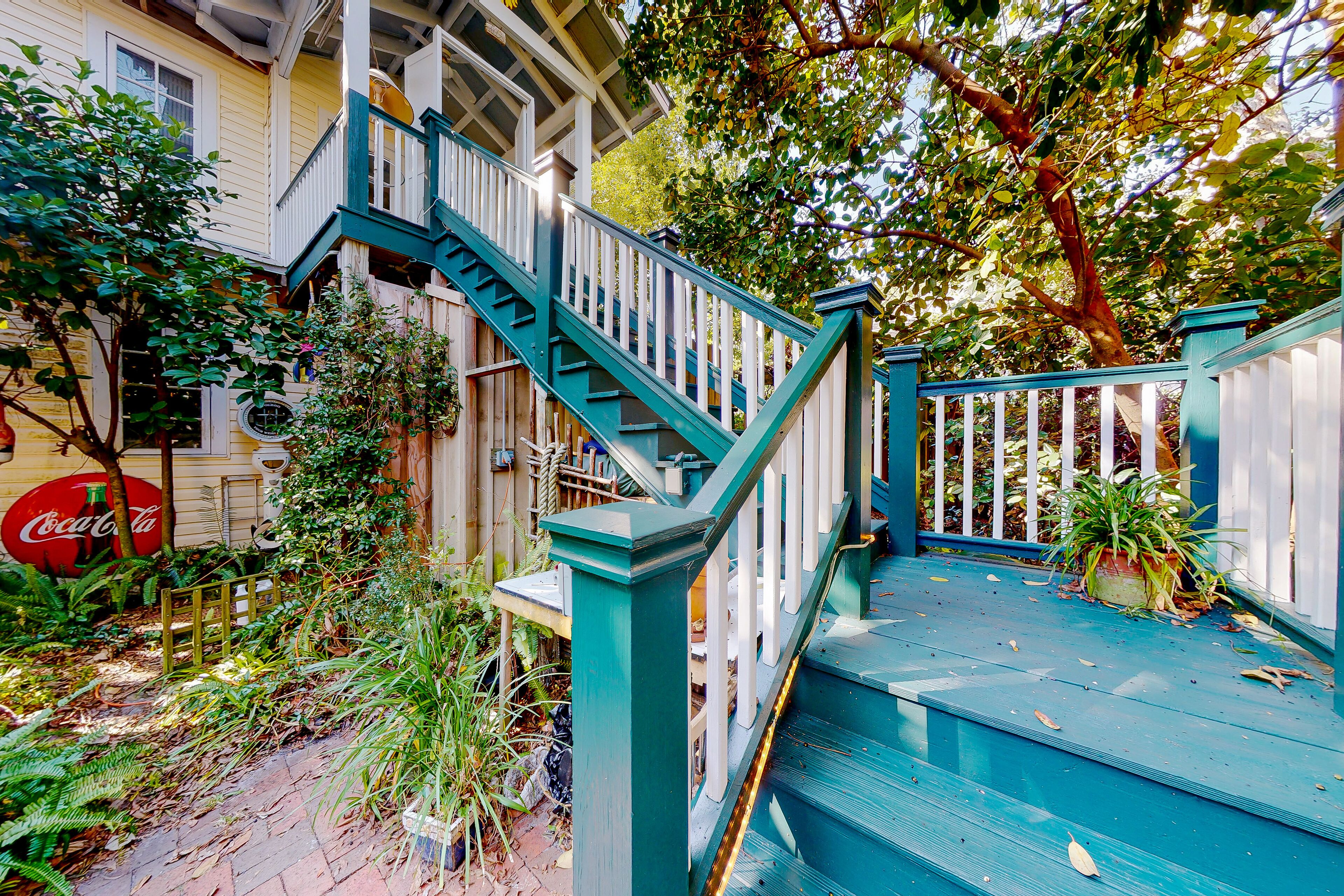 A staircase with teal railings leading to a porch area, surrounded by greenery and a Coca-Cola sign.