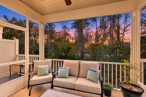 A covered porch with a cushioned seating area, a small table, and a potted plant. - Cozy Island Townhouse W/screened Porch, Shared Pool, & Serene Pond Views (St. Simons Island)