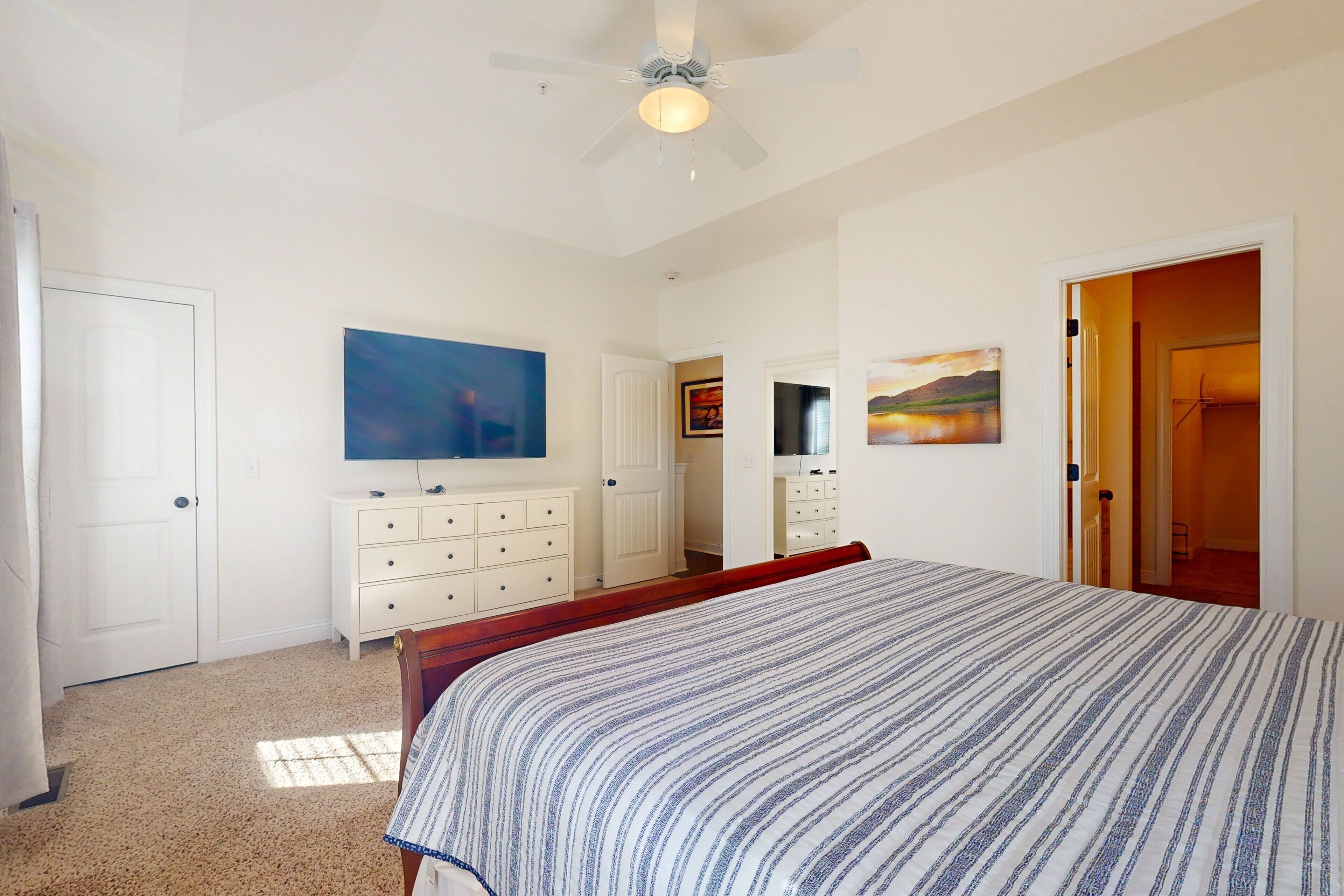 Um quarto com cama, cômoda, ventilador de teto e um quadro na parede.