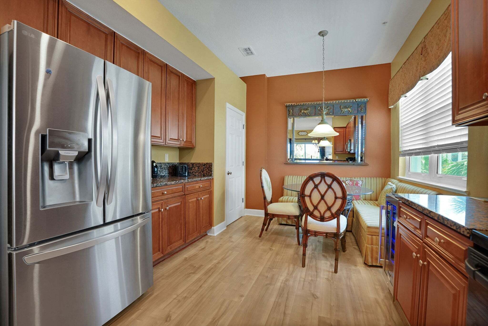 A kitchen with wooden cabinets, a stainless steel refrigerator, a dining table with chairs, and a window with blinds.