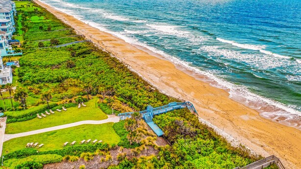 An aerial view of a coastal hotel with a beach, a golf course, and a blue staircase leading to the beach. - Coastal Gem on the Golf Course w/ Shared Pool, & Beach Access - Dog-friendly (Palm Coast)