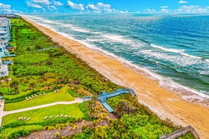 An aerial view of a coastal hotel with a beach, a golf course, and a blue staircase leading to the beach. - Coastal Gem on the Golf Course w/ Shared Pool, & Beach Access - Dog-friendly (Palm Coast)