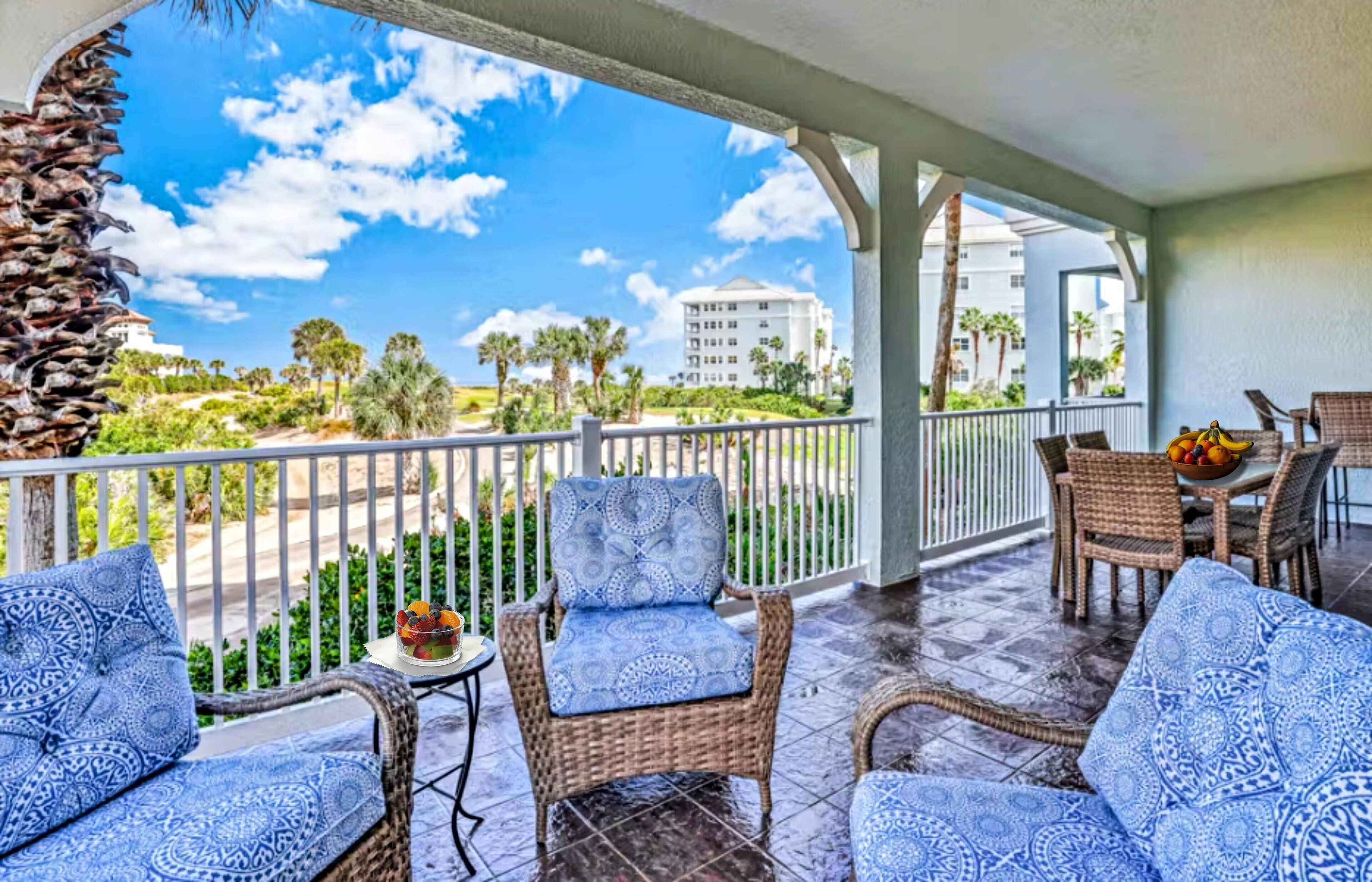 A covered outdoor area with wicker furniture and a view of a building and palm trees.