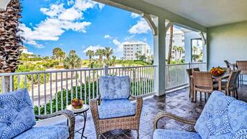 A covered outdoor area with wicker furniture and a view of a building and palm trees.