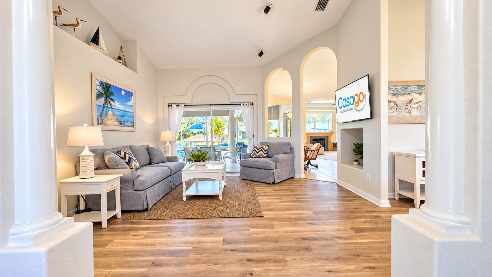 A spacious living room with a grey sofa, a white coffee table, and a view of the outdoors through large windows.
