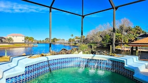 A pool area with a clear view of a large outdoor pool and a smaller hot tub, surrounded by a metal fence and various plants. - Captain's Key Waterside Retreat - Boat Dock! Awesome Pool! (Palm Coast)