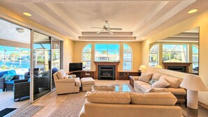 A spacious living room with a fireplace, comfortable seating, and large windows offering a view of the outside. - Captain's Key Waterside Retreat - Boat Dock! Awesome Pool! (Palm Coast)