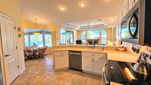 A spacious kitchen with a dishwasher, stove, and a dining area with a view of the outdoors. - Captain's Key Waterside Retreat - Boat Dock! Awesome Pool! (Palm Coast)