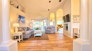 A spacious living room with a wooden floor, two grey sofas, a coffee table, and a fireplace. - Captain's Key Waterside Retreat - Boat Dock! Awesome Pool! (Palm Coast)