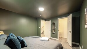 Una camera da letto con un letto, cuscini, una lampada da comodino, uno specchio e una porta che dà su un bagno.
